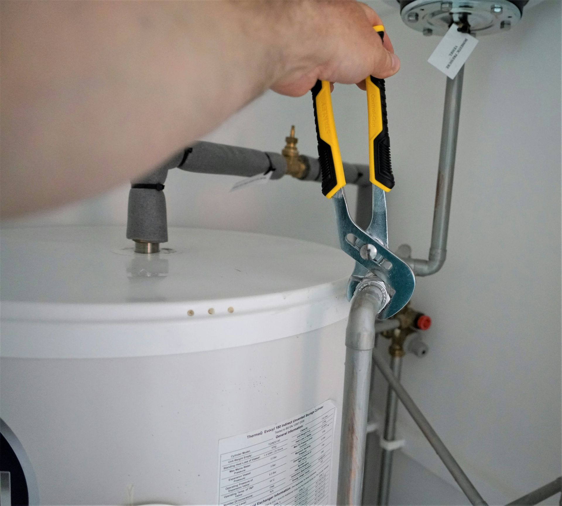 Handwerker zieht mit einer Rohrzange eine Verschraubung an einem Warmwasserspeicher an