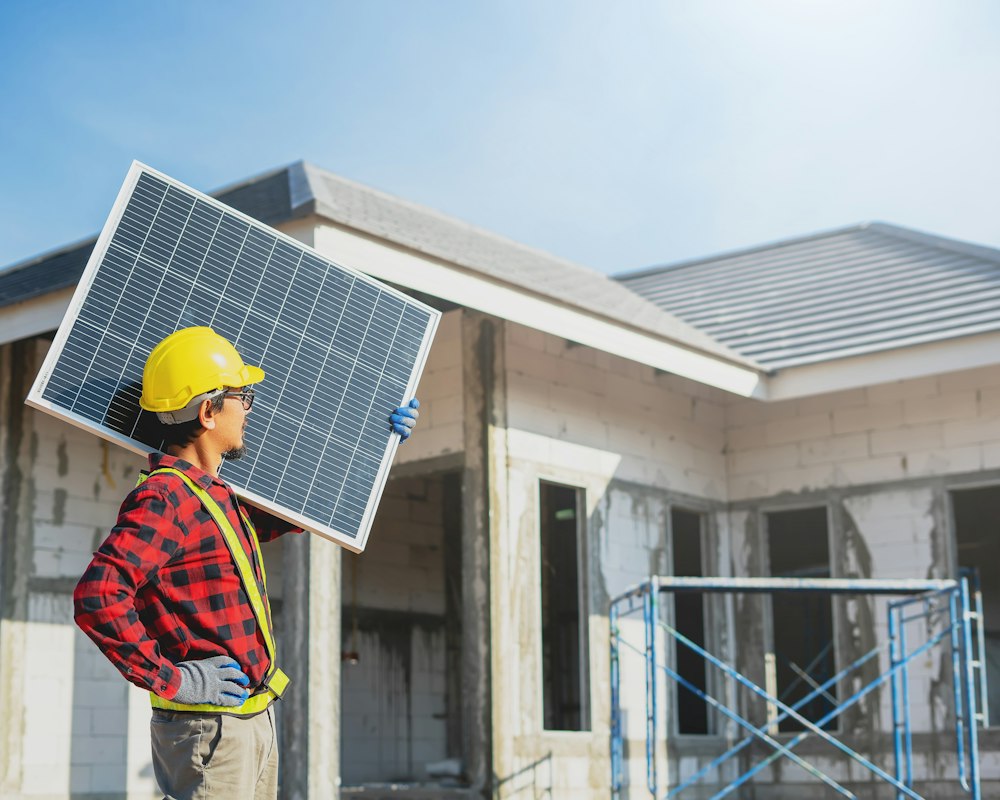 Handwerker mit Fotovoltaik-Modul vor einem Wohnhaus