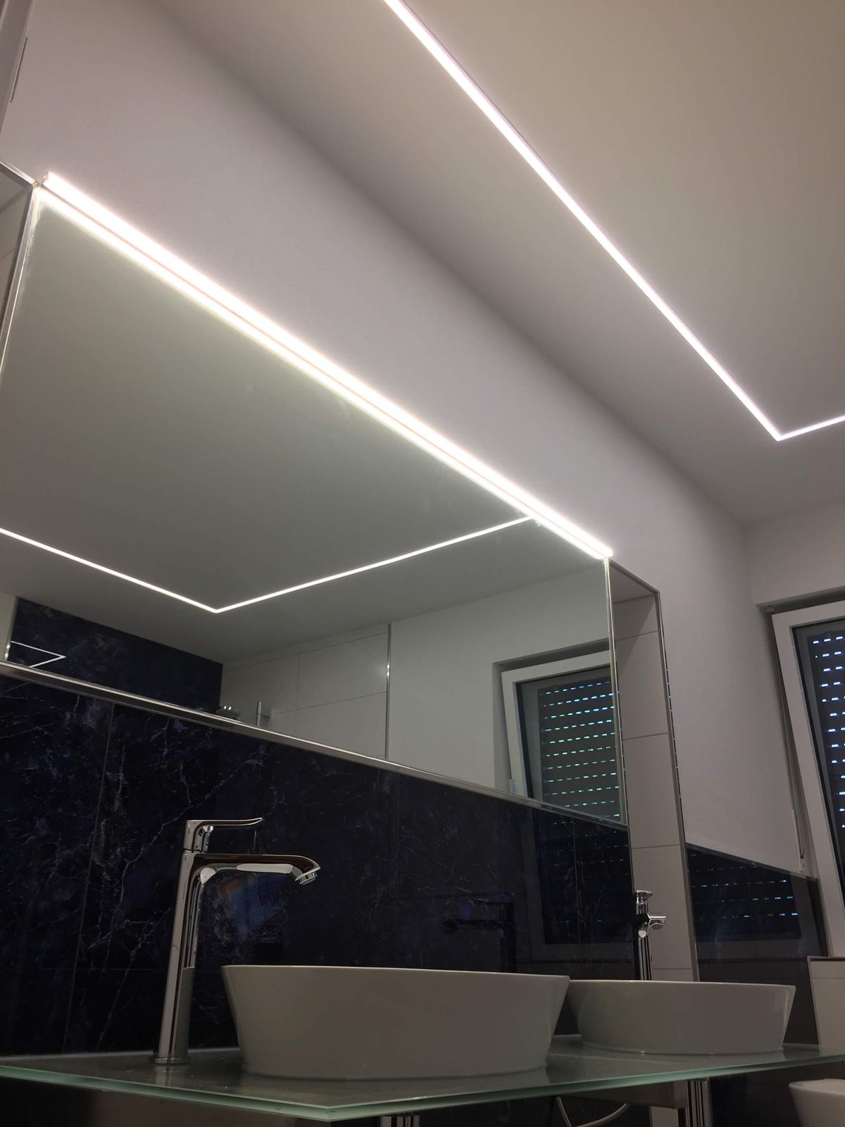 Umlaufendes LED-Lichtband der abgehängten Decke über dem Duschbereich mit dunklen Glasfliesen