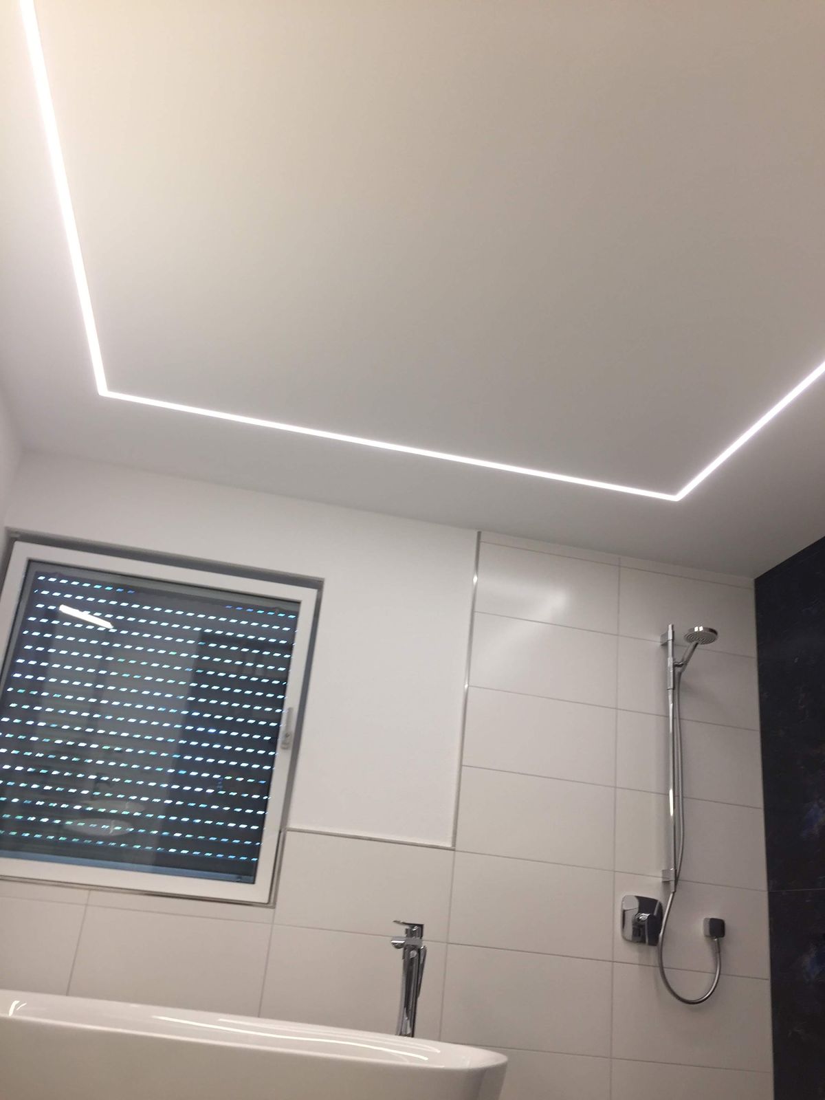 Große deckenbündige Regenbrause in der abgehängten Decke, daneben das umlaufende LED-Lichtband
