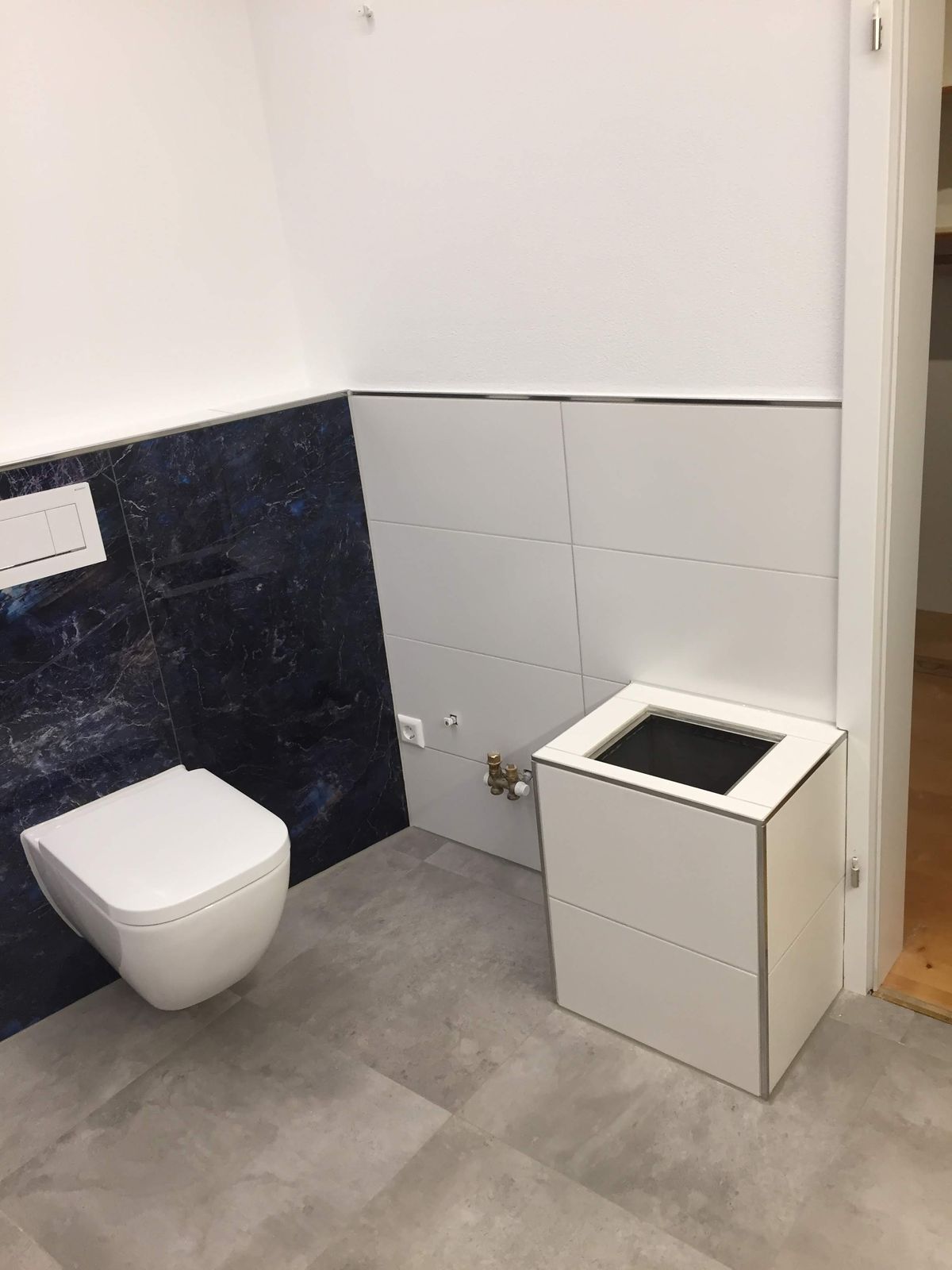 Wandhängendes WC vor weißer Fliesenwand mit dunklen Glasfliesen am Boden