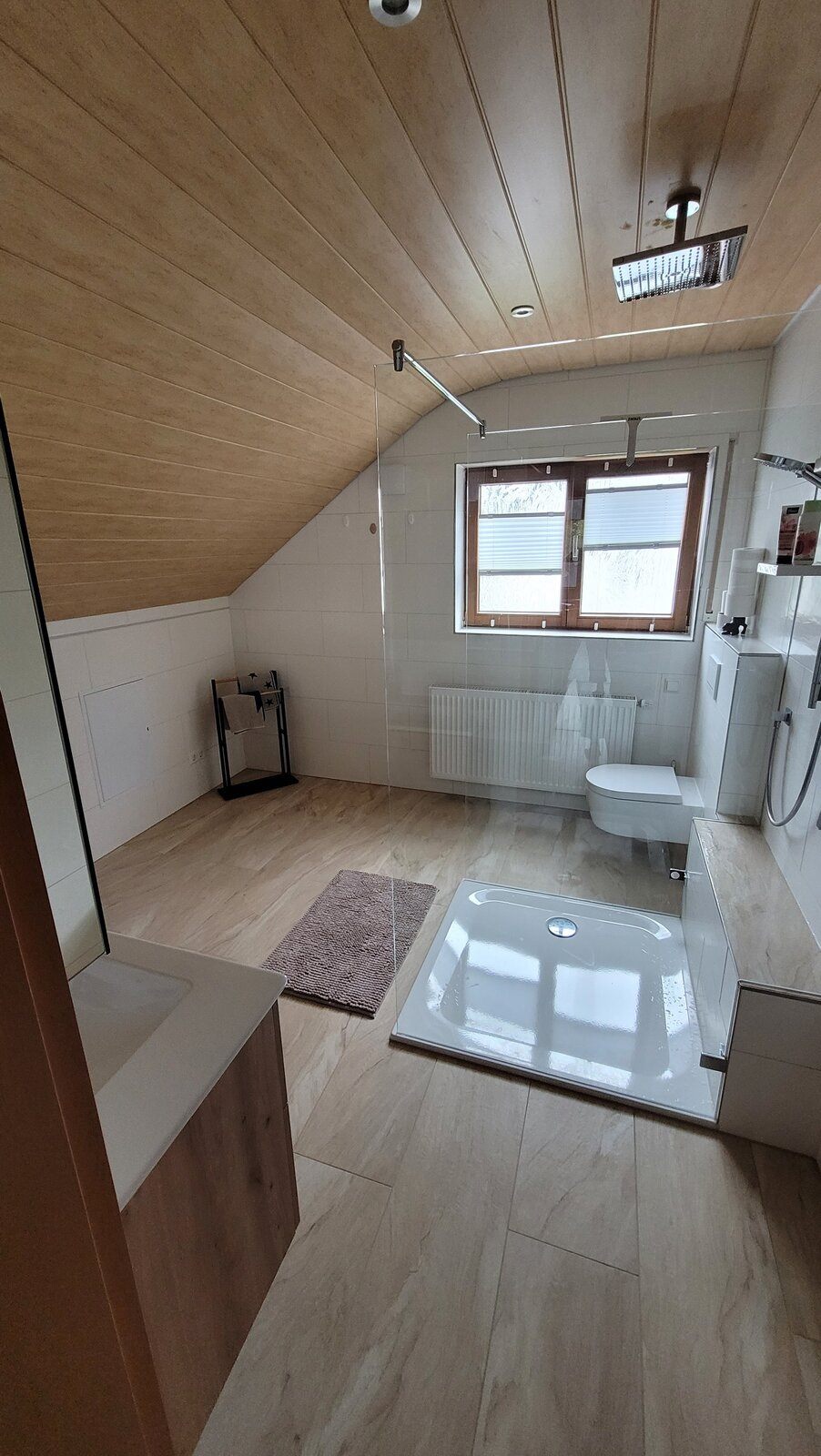 Dachgeschossbad mit holzverkleideter Dachschräge, Fliesen in Holzoptik und freistehender Dusche
