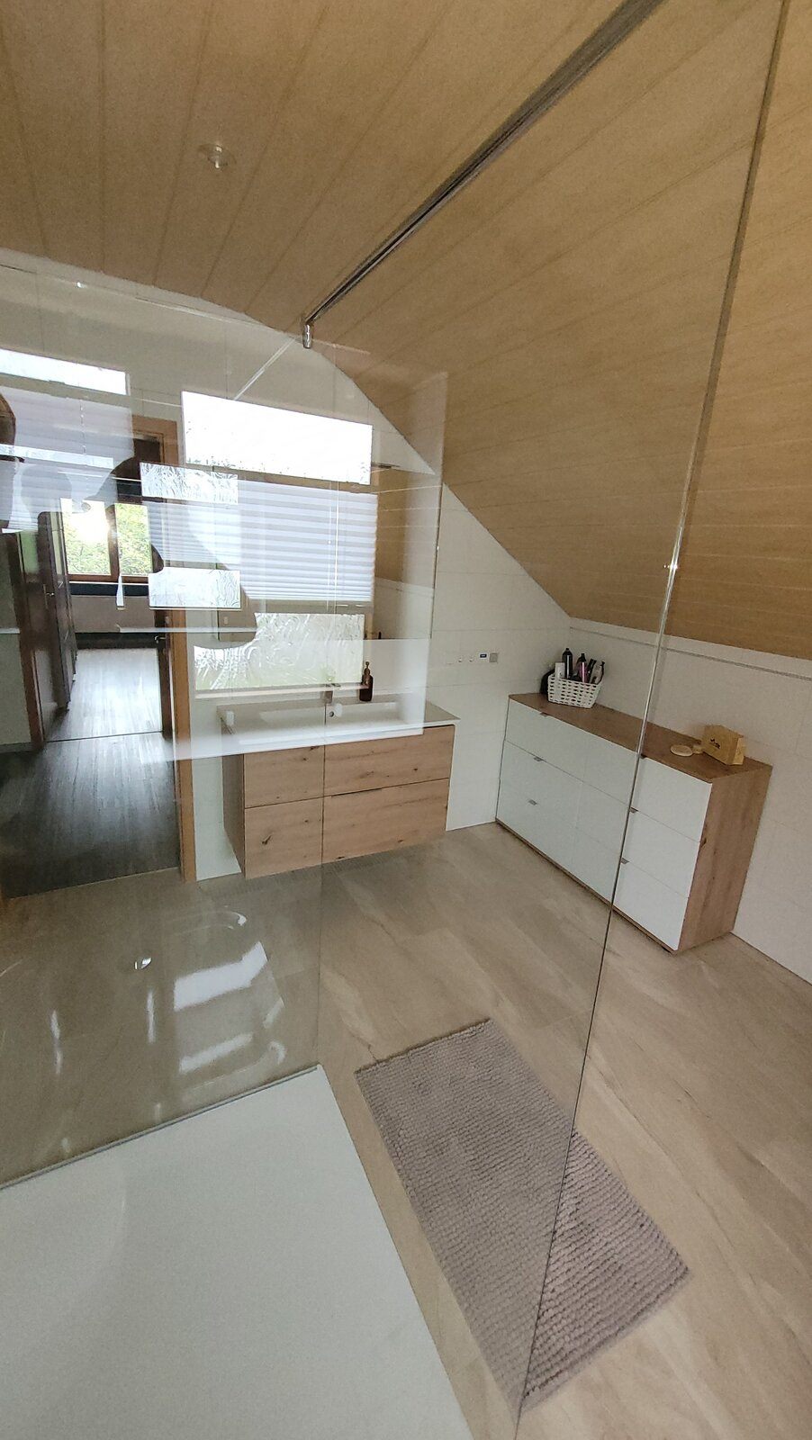 Blick über die Duschfläche auf Waschtisch und Sideboard unter der Dachschräge