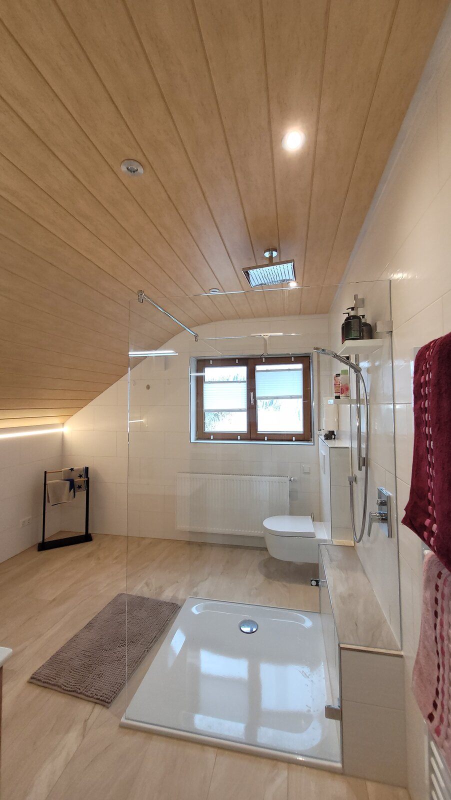 Deckenmontierte Regenbrause über der flachen Duschwanne, dahinter Fenster und Wand-WC