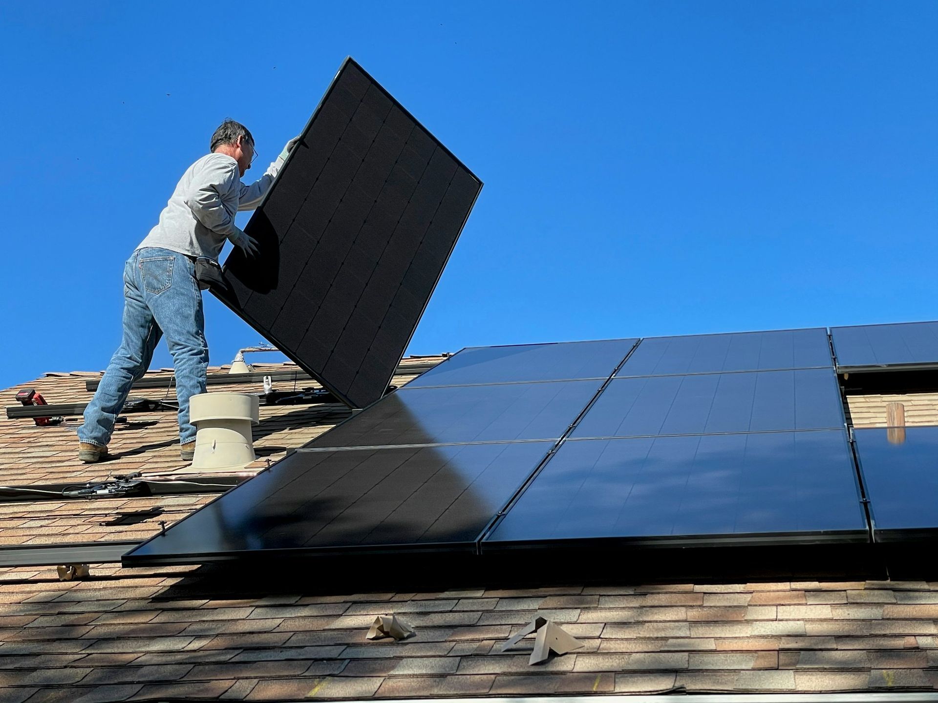 Handwerker montiert Solarmodule auf einem Hausdach vor blauem Himmel